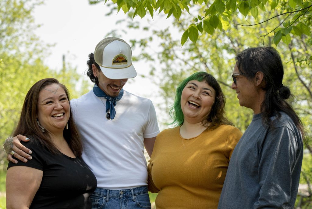 Four people laughing together outdoors in a leafy park